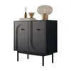 A black cabinet with gold handles and decorative arches on the doors, placed on thin black legs. It is decorated with a lamp, a bowl, and a bottle of diffuser on top. Produktbild-Vorschau