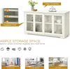 A white kitchen sideboard with glass sliding doors, displaying kitchenware and decorative items. The image also includes text overlays highlighting features and different room placements. Podgląd zdjęcia produktu