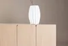 A white vase with a twig sits on top of a light wood cabinet. Produktbild-Vorschau