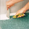 A person is using a utility knife to cut a piece of teal carpet near a white baseboard. Produktbild-Vorschau