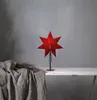A red star-shaped lamp sits on a white table next to a draped gray cloth. Podgląd zdjęcia produktu