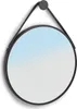 A round mirror with a black frame and a black strap hanging from a hook.
