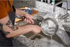 A person is washing a pot in a sink with a brush. Voir les images du produit