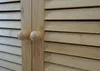 Close-up of a wooden cabinet with louvered doors and round wooden knobs. Náhľad obrázku produktu
