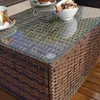 A close-up view of a polyrattan coffee table with a glass top, showing a cup of tea and cookies. Náhled obrázku produktu