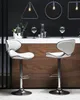 Two white bar stools are placed in front of a wooden bar counter with a black wall behind it. There are decorative items on the counter. Náhled obrázku produktu