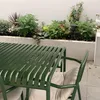 An outdoor patio setting with a green metal table and chairs, surrounded by plants and a white wall. Produktbild-Vorschau