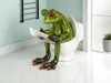 A green frog figurine sits on a toilet and reads a newspaper. Produktbild-Vorschau