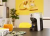 A coffee machine and a jug of juice are on a table, with a yellow telephone artwork in the background. Produktbild-Vorschau