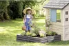 A young girl is playing in a garden next to a playhouse and a raised garden bed. Voir les images du produit