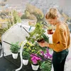 A woman is tending to plants in a small greenhouse on a balcony. Voir les images du produit