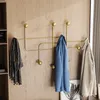 A gold metal coat rack mounted on a light wood paneled wall, with a scarf, a blue sweater, and a beige sweater hanging on it. Voir les images du produit