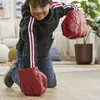 A young boy wearing a black hoodie with red and white stripes on the sleeves and blue jeans, kneeling on a wooden floor. He is wearing large red Hulk-like gloves on both hands and looking at the camera with a smile. In the background, there is a couch, a p Anteprima dell’immagine prodotto