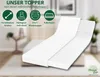 A white mattress topper is shown on a bed in a room, with marketing icons and text overlayed. Produktbild-Vorschau