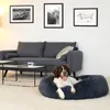 A dog is resting in a donut-shaped dog bed in a living room. Anteprima dell’immagine prodotto
