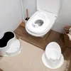 A bathroom scene with a toilet, a child's toilet seat, and a potty. Produktbild-Vorschau