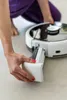 A person's hands are shown inserting a white component into a white and black robotic vacuum cleaner. Produktbild-Vorschau