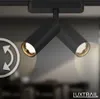 Close-up of two black track light fixtures with gold interiors, mounted on a black track. An arrow graphic indicating rotation is superimposed on the left side of the image. The LuxTrail logo is visible in the bottom right corner. Produktbild-Vorschau