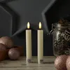Two LED candles with a rustic look are placed on a wooden surface, surrounded by decorative Christmas ornaments and pine cones in a jar. Produktbild-Vorschau
