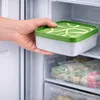 A hand is placing a square food container with a green lid into a freezer. Produktbild-Vorschau