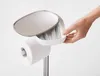 A hand is shown reaching into a compartment of a toilet paper stand. Voir les images du produit