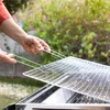 A person is placing a metal grill rack onto a barbecue. Produktbild-Vorschau