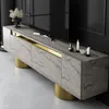 A modern TV cabinet with a marble-like finish and gold accents, placed in a dimly lit room with a large black television in the background. Produktbild-Vorschau