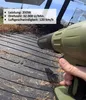 A hand holding a green leaf blower on a wooden surface with some dry leaves. Produktbild-Vorschau