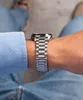 A close-up shot of a person's wrist wearing a silver watch and a blue shirt. Produktbild-Vorschau