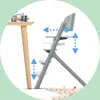 A high chair is shown next to a table leg, with arrows indicating adjustable height and position features. Some wooden toy pieces are on the floor. Podgląd zdjęcia produktu