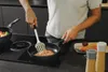 A person is cooking salmon in a frying pan on a stovetop. Produktbild-Vorschau