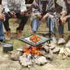 People are sitting around a campfire with a grill over the fire, cooking skewers of vegetables. Náhled obrázku produktu