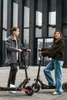 A man and a woman stand with electric scooters in front of a modern building. Náhled obrázku produktu