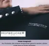 A close-up of a person's arm resting on a dark fabric, with branding visible. Produktbild-Vorschau