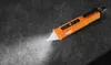An orange and black voltage tester with its light on, lying on a dark, textured surface. Podgląd zdjęcia produktu