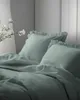 A close-up view of a bed with mint-colored bedding and pillows, featuring ruffled edges. A branch with white flowers is visible on the left side. Produktbild-Vorschau