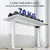 A white electric standing desk with weights on top and the text '70 KG' prominently displayed. The background shows blinds and sheer curtains. Voir les images du produit