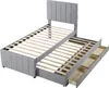 A grey upholstered bed frame with a headboard and a pull-out trundle bed with drawers underneath, shown from a diagonal angle against a white background. Produktbild-Vorschau