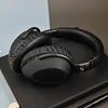 A pair of black over-ear headphones rests on a dark surface, with a blurred background. Produktbild-Vorschau