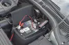 A car battery with jumper cables connected to a battery tester in an engine bay. Náhled obrázku produktu