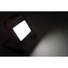 A portable LED work light is shown in a dark environment, illuminating a surface with a bright beam. Produktbild-Vorschau