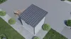 A small, modern garden shed with a gray metal roof is situated on a paved patio area, surrounded by gravel and grass. A lounge chair is visible nearby. Produktbild-Vorschau