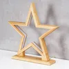 A wooden star-shaped lamp with LED lights sits on a white surface against a gray concrete wall. Produktbild-Vorschau