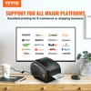 A VEVOR label printer is shown on a desk with a computer monitor displaying various e-commerce platform logos in the background. Podgląd zdjęcia produktu