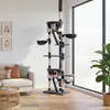 A tall cat tree is shown in a living room setting with a sofa and a large window. Produktbild-Vorschau