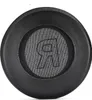A close-up, top-down view of a black headphone earpad with a textured fabric center featuring a raised logo. Podgląd zdjęcia produktu