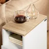 A close-up shot of a bedside table with a cup of coffee and a vase on top. Books are visible in the open shelf below. Voir les images du produit
