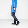 A person wearing a blue coat and jeans, standing on a white surface, wearing blue Birkenstock sandals. Produktbild-Vorschau