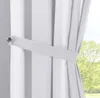 A close-up view of a white curtain held back by a tie-back, with a blurred green tree visible through a window in the background. Produktbild-Vorschau