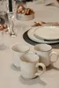 A table setting with three ceramic mugs, plates, cutlery, and decorative elements. Náhľad obrázku produktu
